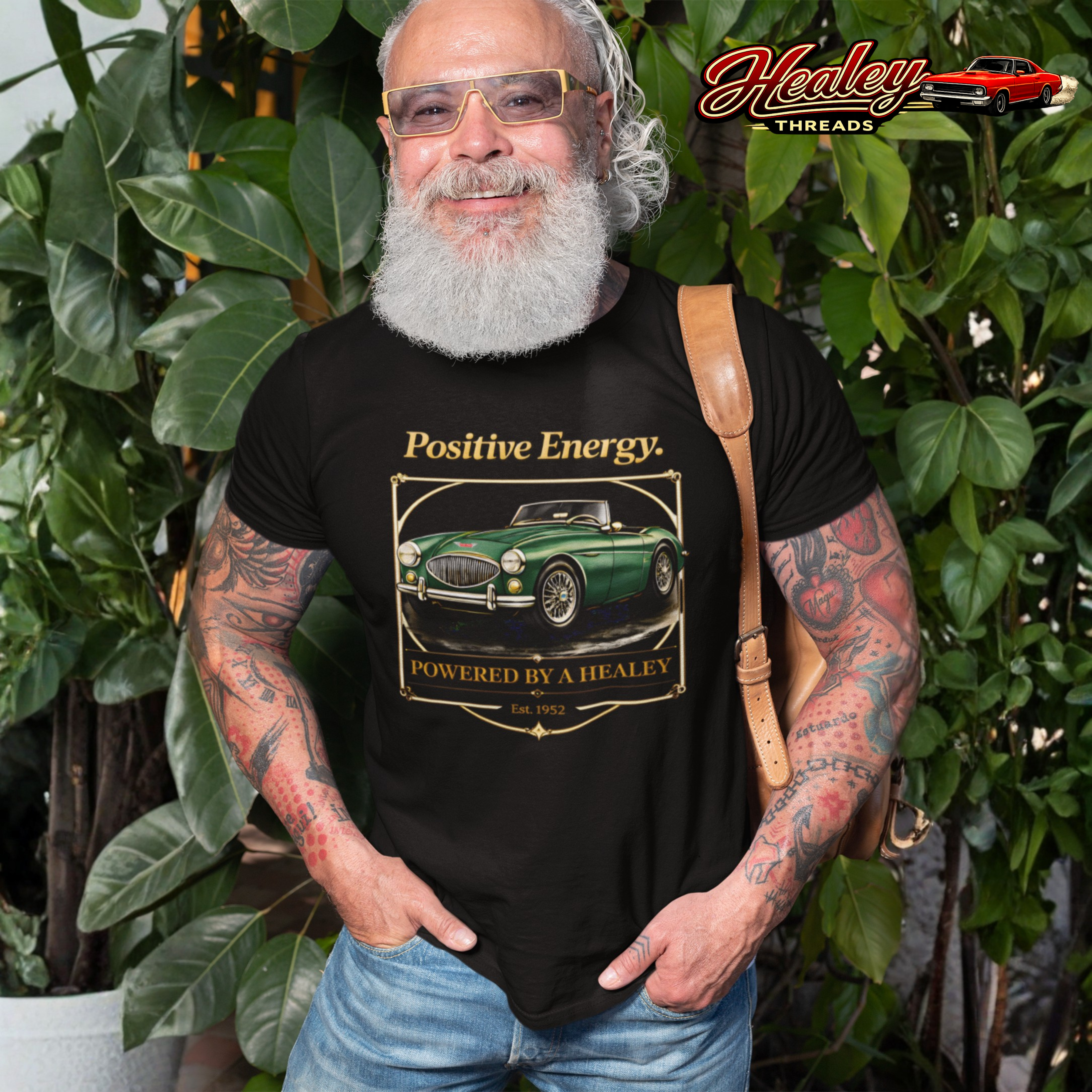 Man wearing a black t-shirt with a classic car graphic and 'Positive Energy' text, standing outdoors with greenery.
