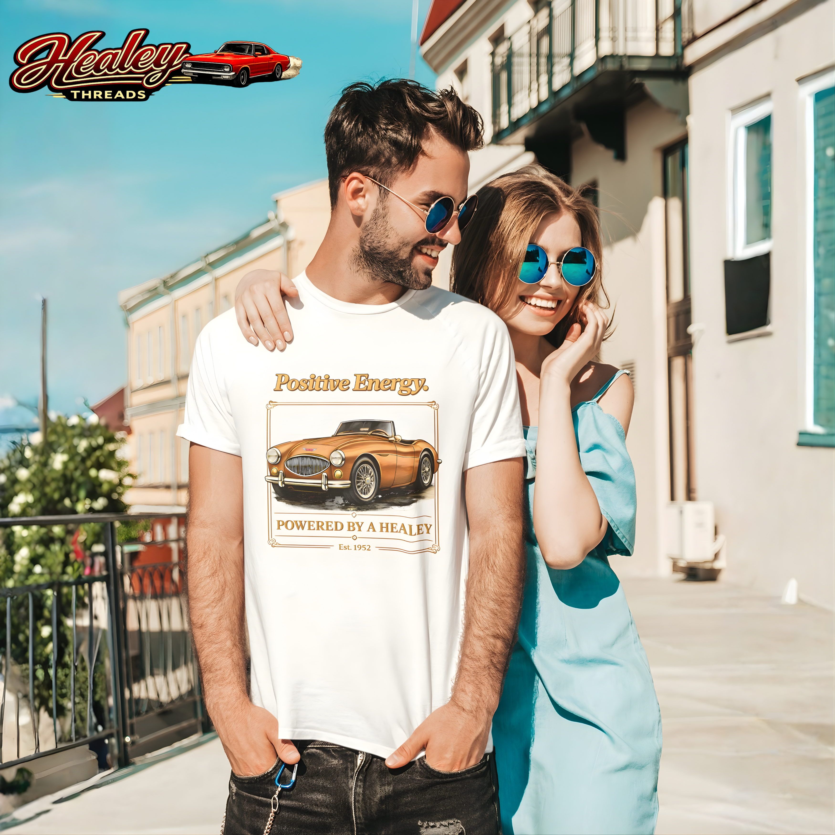 Man and woman standing together on a sunny street, with the man wearing a white t-shirt featuring a classic car design.