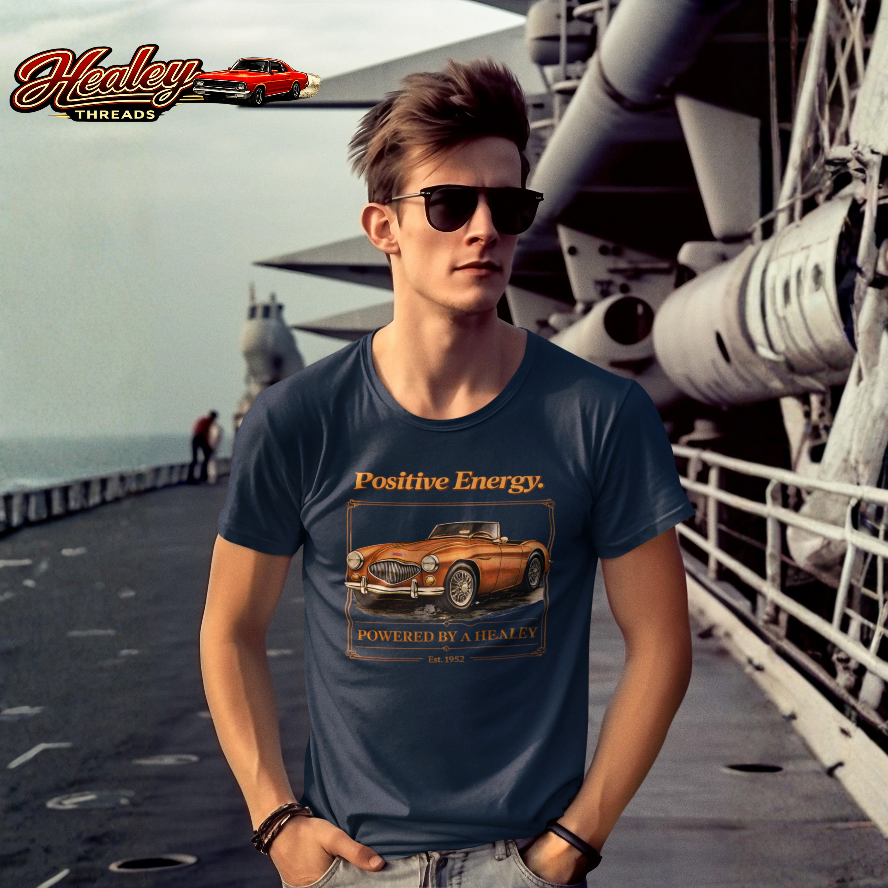 Man wearing a navy blue t-shirt with a classic car graphic and 'Healey Threads' branding on a ship deck.