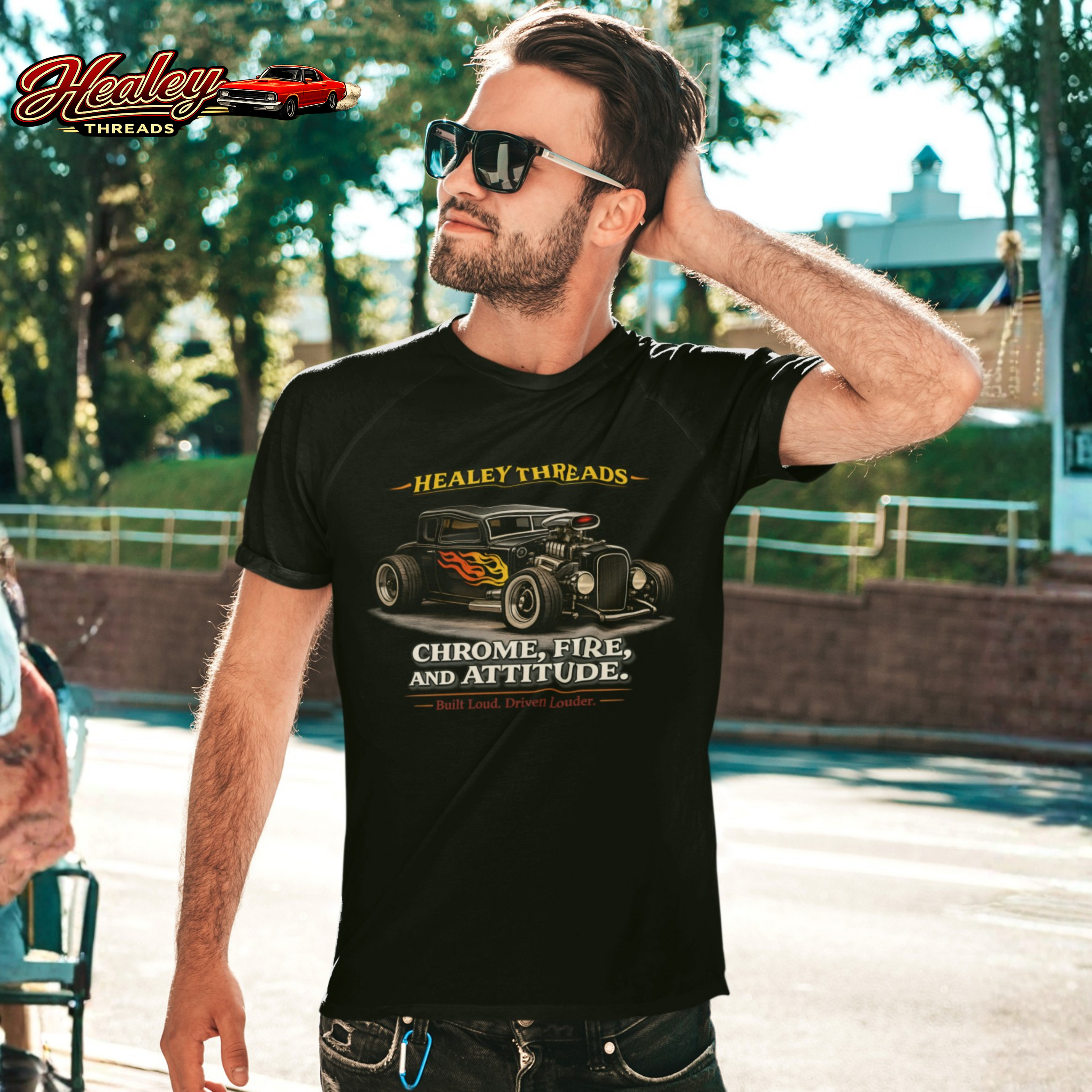 Man wearing a black t-shirt with a hot rod car design and a 'Healey Threads' design outdoors. 