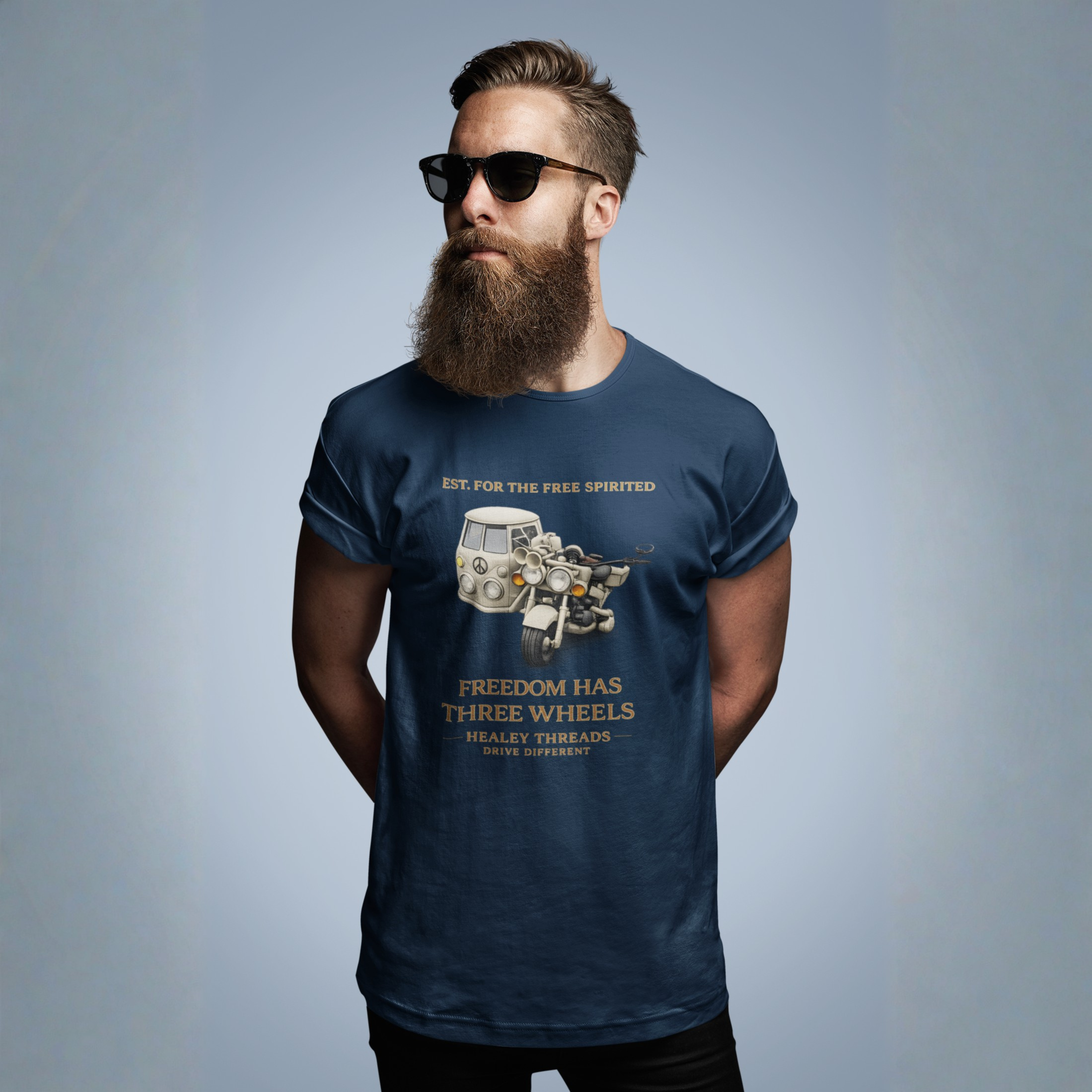 Man wearing a navy blue t-shirt with Cream motorcycle-sidecar van mashup with peace symbol and gold "Freedom Has Three Wheels" text on a blue background