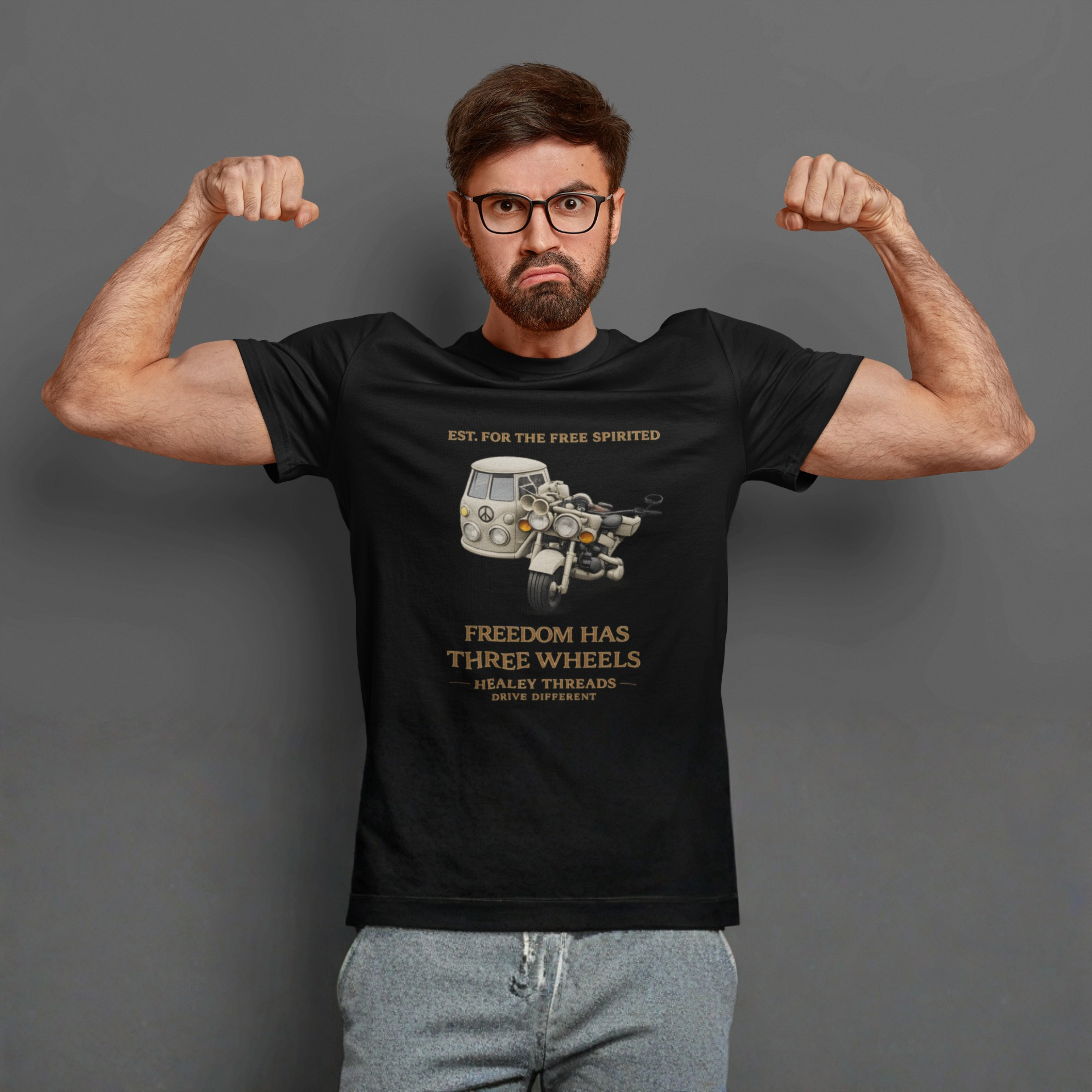 Man wearing a black t-shirt with Cream motorcycle-sidecar van mashup with peace symbol and gold "Freedom Has Three Wheels" text  flexing his muscles against a gray background