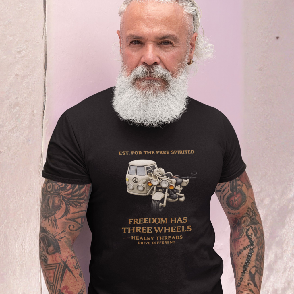 Man wearing a black t-shirt with a tri bike motorcycle and a sidecar graphic and text, standing against a light pink wall.