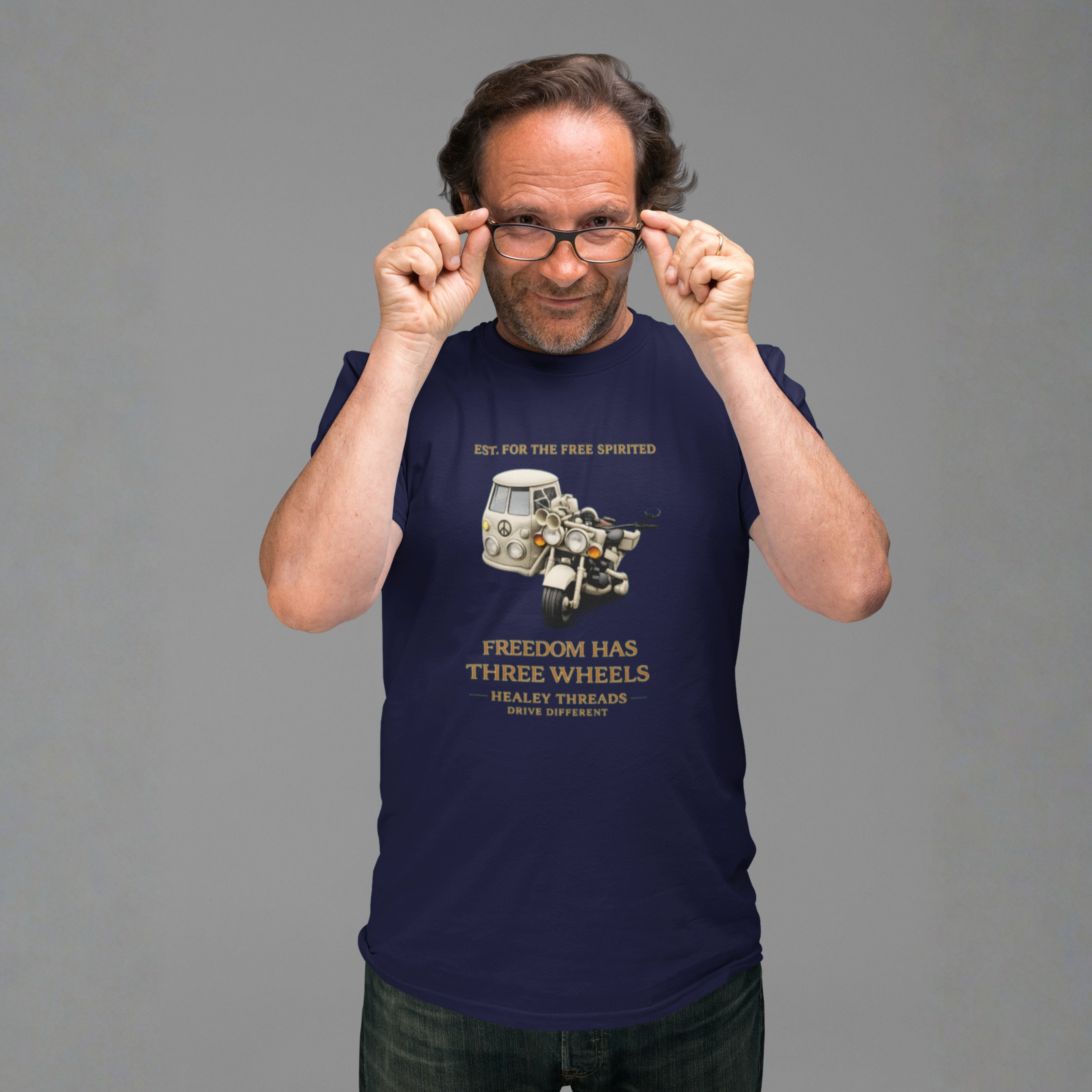 Man in navy tee with vintage motorcycle-van mashup graphic and gold 'Freedom Has Three Wheels' text