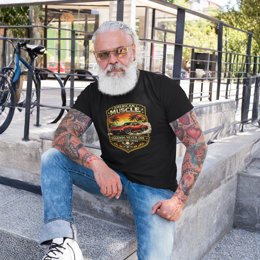 Man with tattoos wearing a black t-shirt with a graphic classic car design, sitting on steps outdoors.