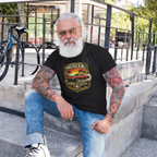 Man with tattoos wearing a black t-shirt with a graphic classic car design, sitting on steps outdoors.