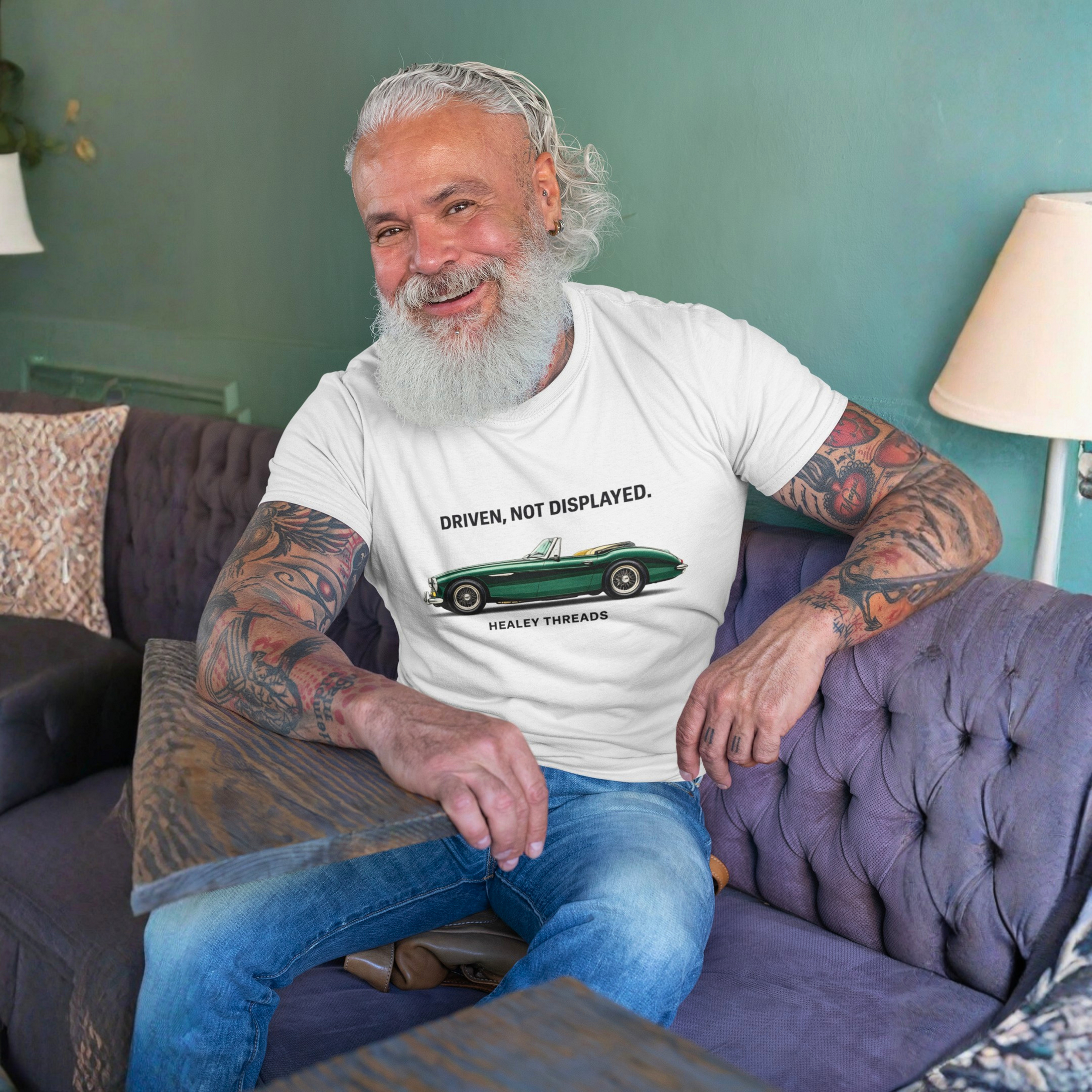 Man sitting on a couch wearing a white t-shirt with a classic car graphic design and text.