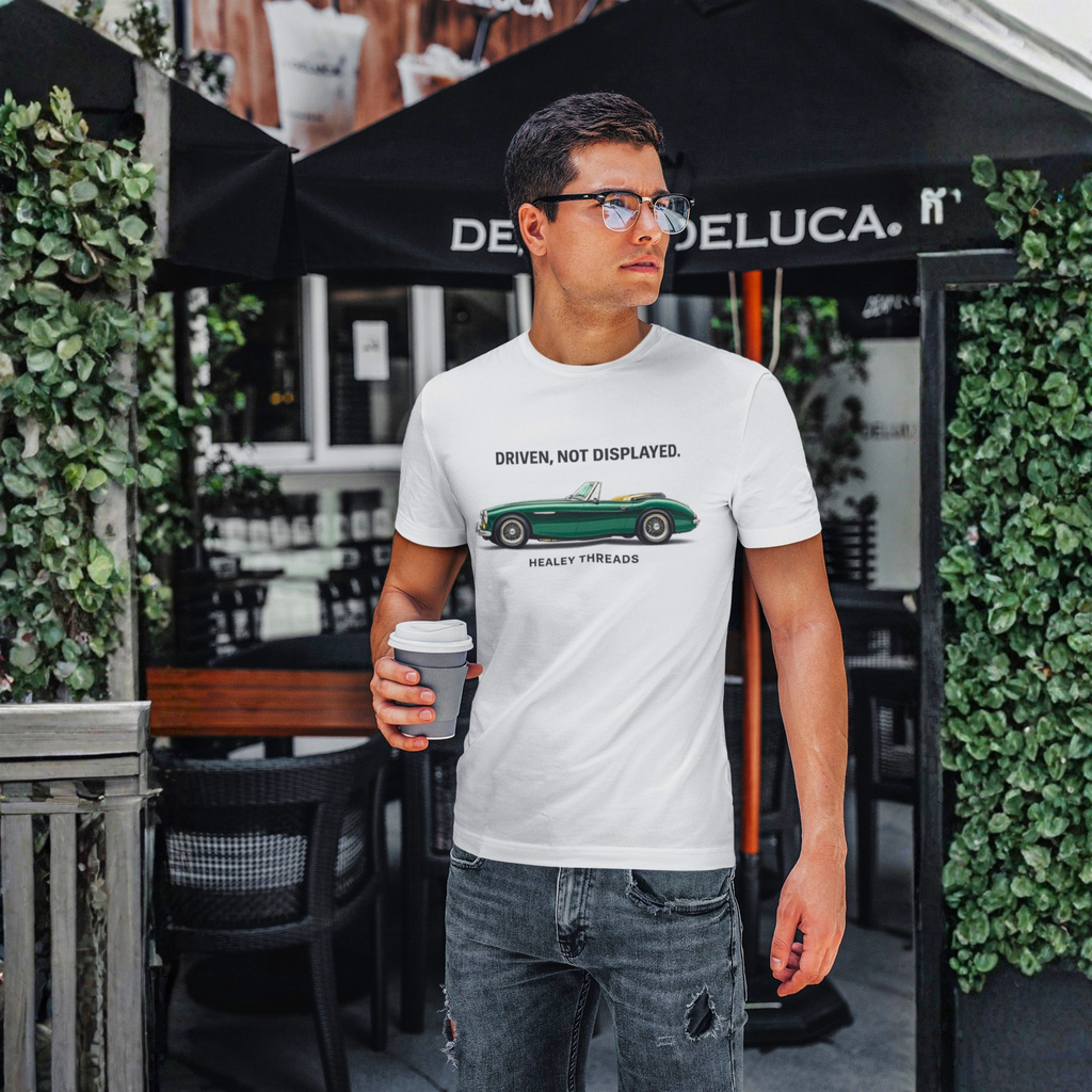 Man wearing a white t-shirt with a classic car graphic design, holding a coffee cup, standing in front of a Deluca umbrella.