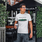 Man wearing a white t-shirt with a classic car graphic design, holding a coffee cup, standing in front of a Deluca umbrella.