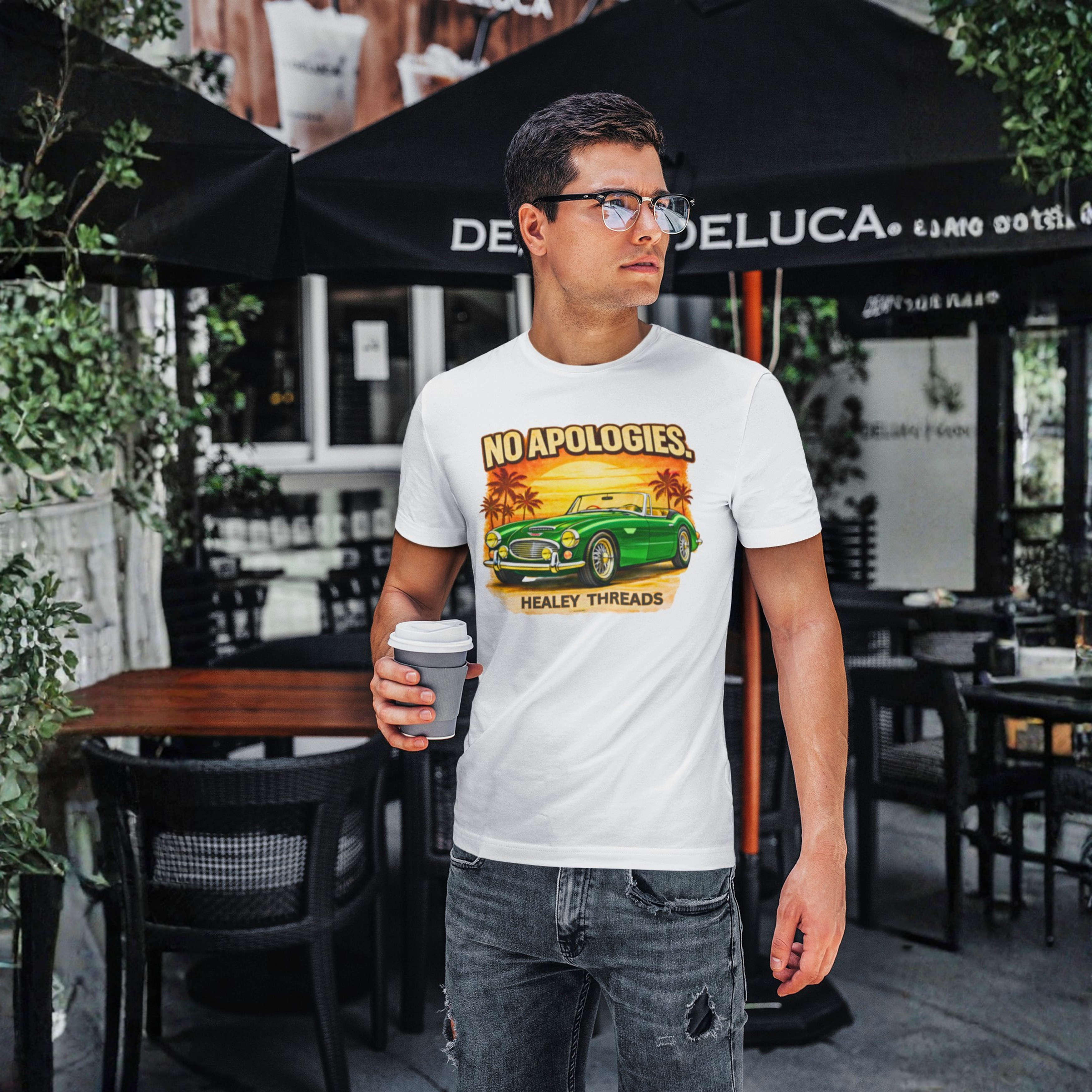 Man wearing a white t-shirt with a graphic design of a vintage Healey car and text, standing in an outdoor cafe setting.