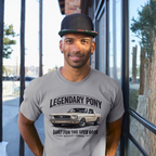 Man wearing a gray t-shirt with a classic car graphic and text, standing in front of a glass door.