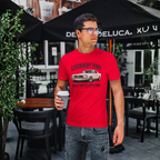 Man wearing a red t-shirt with a classic car graphic and text, standing outdoors under a black umbrella.