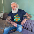 Man with tattoos wearing a navy blue t-shirt with colorful van graphics and text, sitting on a couch.