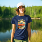 Woman wearing a navy blue t-shirt with a graphic design of a van and palm trees, standing by a lake with greenery in the background.