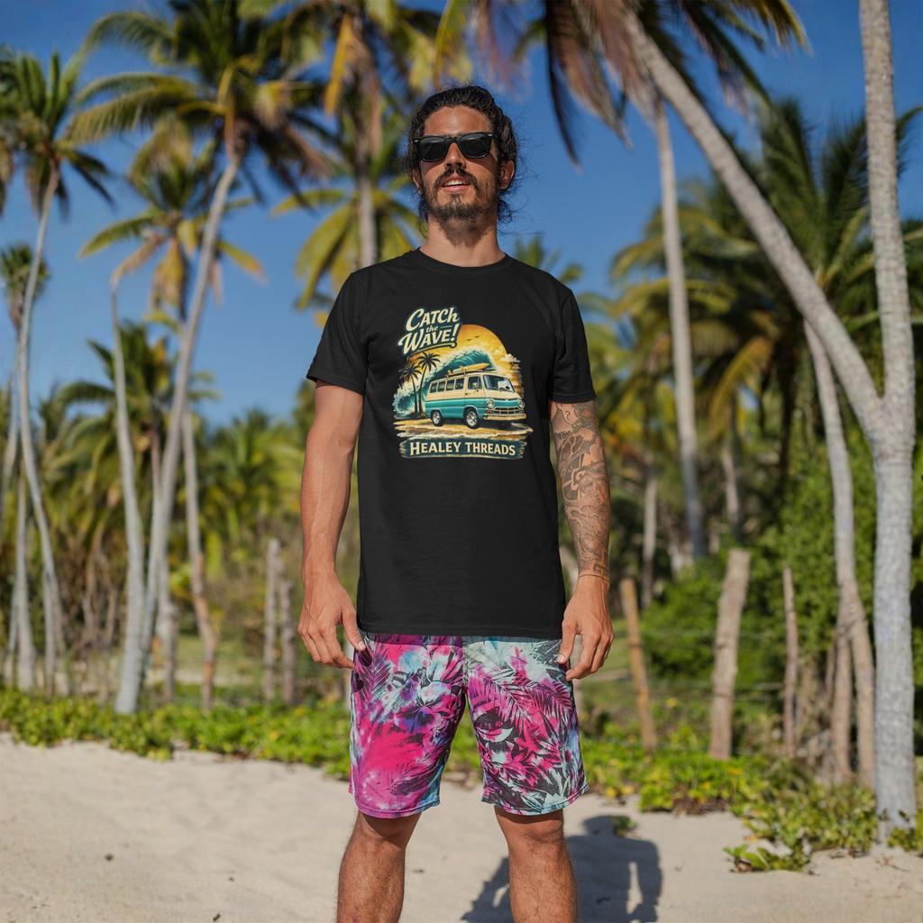 Man wearing a black t-shirt with a graphic Mopar van design and colorful shorts standing on a beach with palm trees in the background.