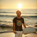 Man holding a surfboard on a beach at sunset, wearing a Black t-shirt flat lay featuring a retro surf van beach graphic with palm trees and a sunset, reading "Sun. Salt. Air., Coastal Cruisers, Healey Threads."