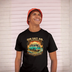 Person wearing a black t-shirt with a graphic van design and text, standing against a light wooden panel background.