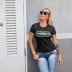 Woman wearing a black t-shirt with a graphic design and text, standing against a gray wall.