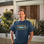 Man wearing a navy blue t-shirt with a graphic Healey and text, standing outdoors.