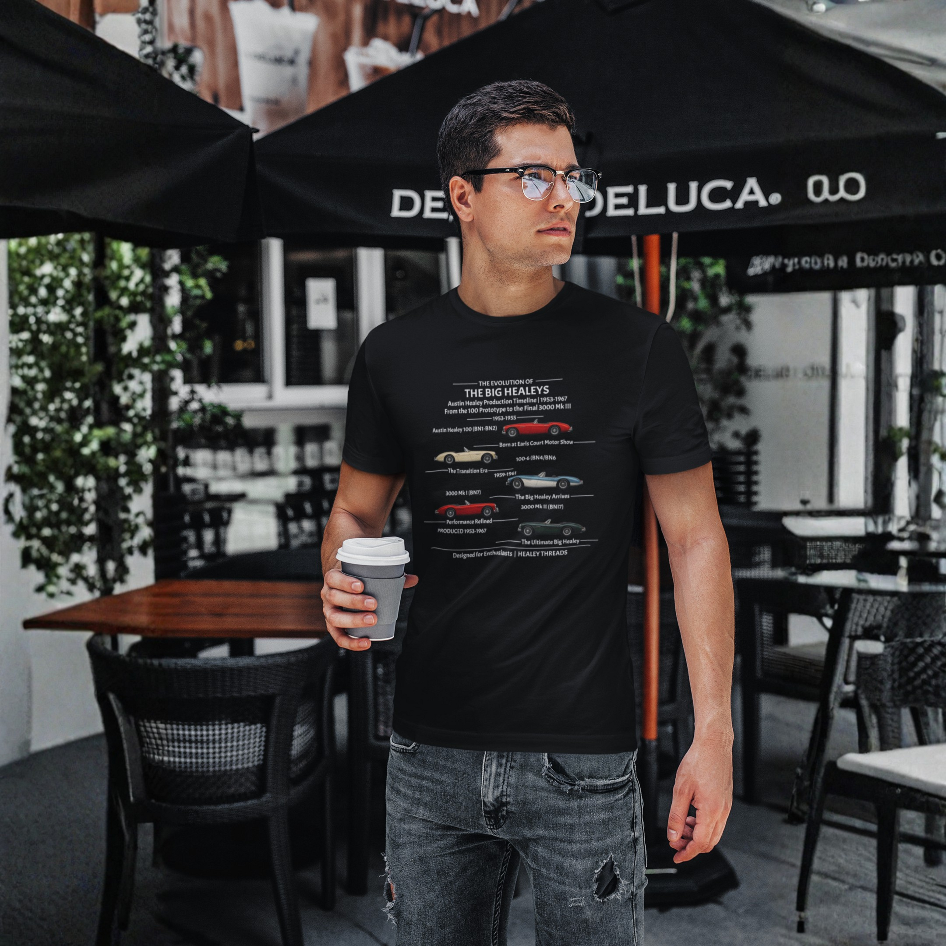 Man wearing a black t-shirt with a Healey timeline graphic design holding a coffee cup