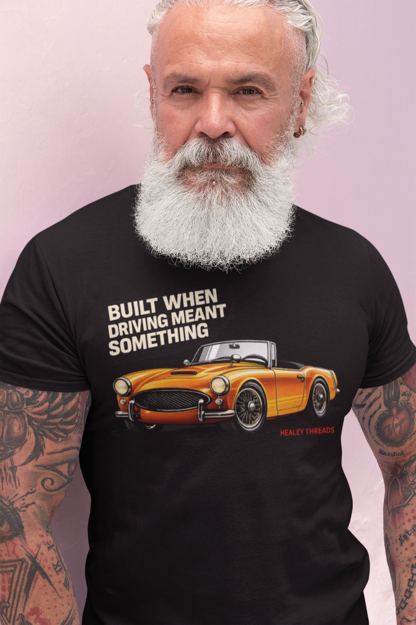 Man wearing a black t-shirt with a British classic car graphic and text on a pink background