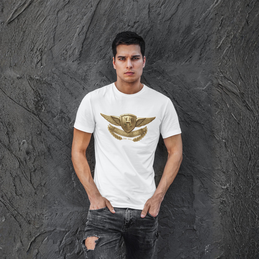 Man wearing a white t-shirt with a gold Healey emblem against a dark textured wall