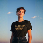 Woman wearing a black t-shirt with a gold Healey emblem against a blue sky.