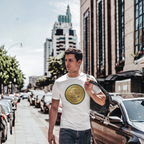 Man walking on a city street wearing a white t-shirt with a a classic car coin design.