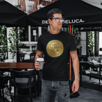 Man wearing a black t-shirt with a gold classic car logo, holding a coffee cup, standing under a Deluca umbrella.