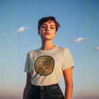 Woman wearing a white t-shirt with a circular classic car logo against a blue sky.