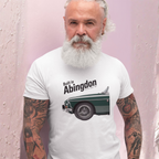 Man wearing a white t-shirt with a classic car graphic and text, standing against a light pink background