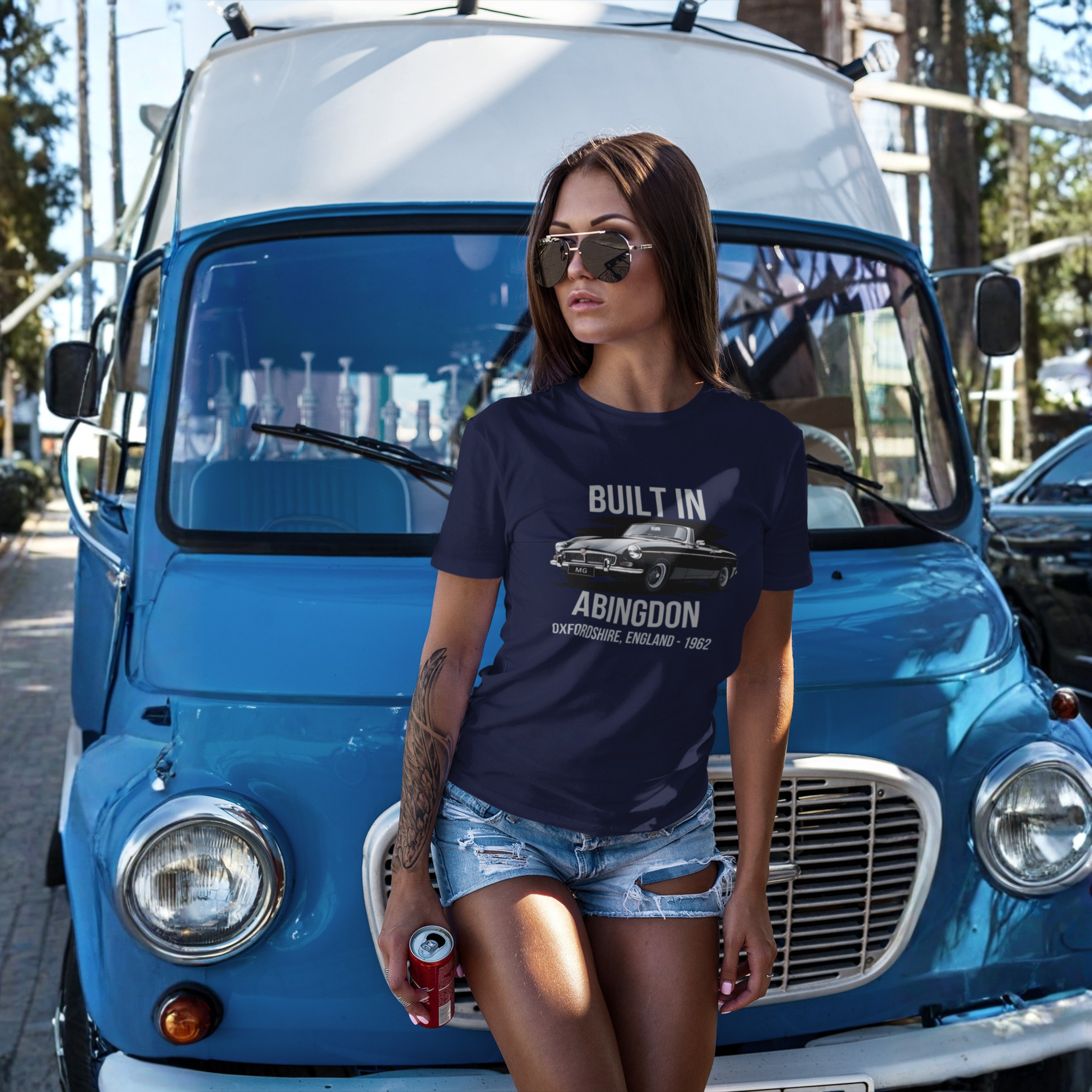 Woman wearing a navy blue t-shirt with classic car graphic design and text, standing in front of a blue van.