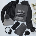 Collection of clothing and accessories including a t-shirt with 'Built in Abingdon' design, black jacket, gray beanie, gloves, jeans, headphones, and a mug on a light background.