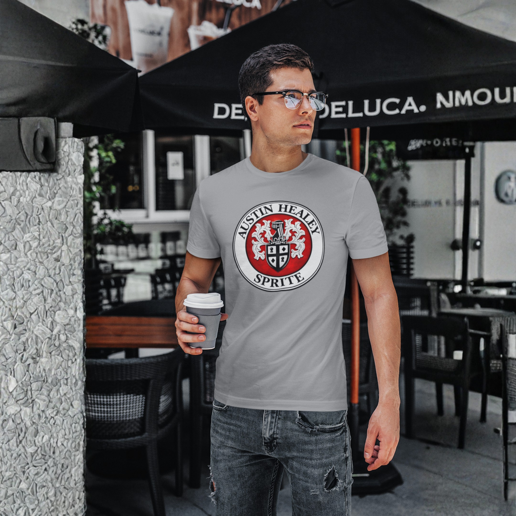 Man wearing a gray t-shirt with a Healey Sprite logo, holding a coffee cup, standing outdoors.