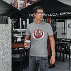 Man wearing a gray t-shirt with a Healey Sprite logo, holding a coffee cup, standing outdoors.