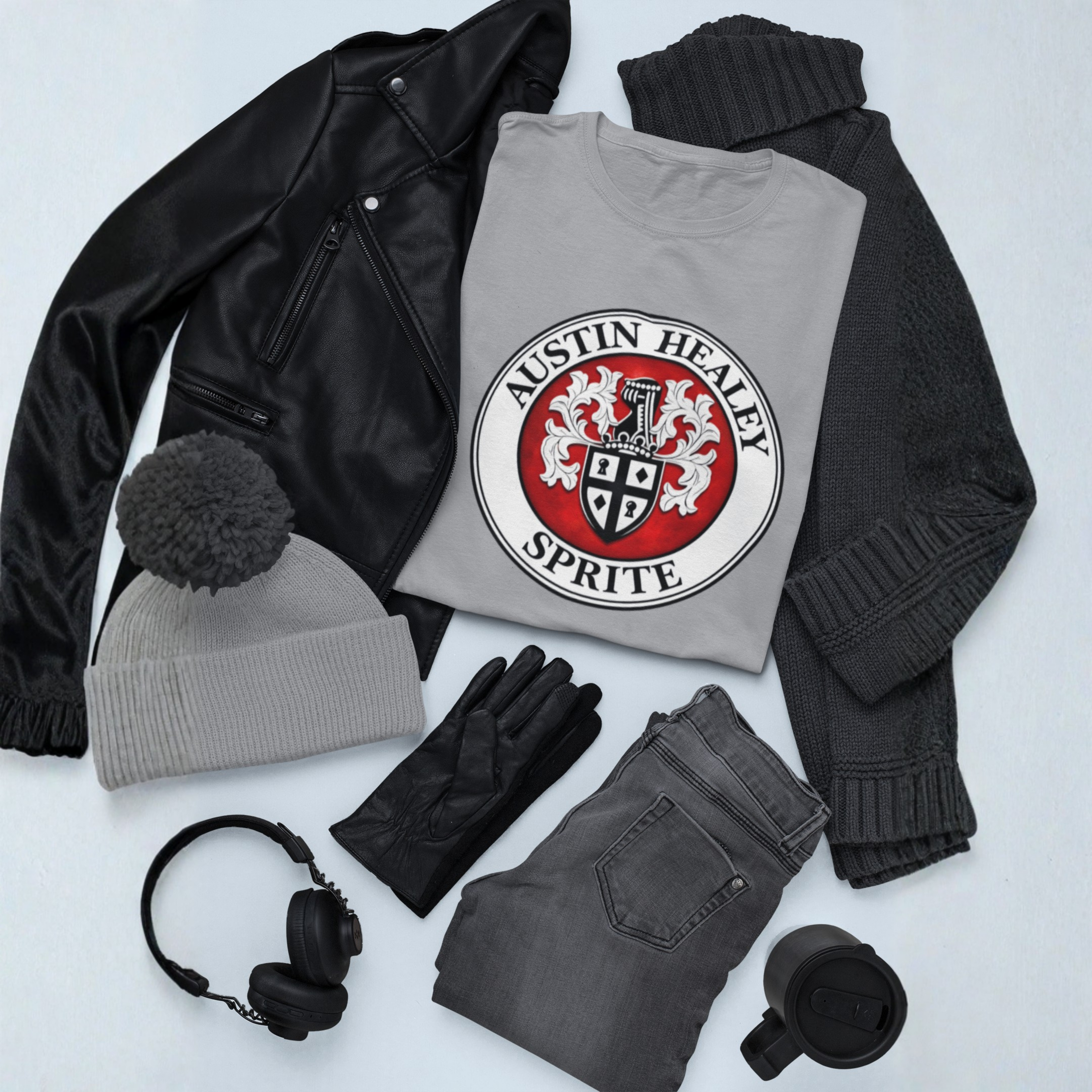 Collection of clothing and accessories including a t-shirt with a Austin Healey Sprite logo, jacket, beanie, gloves, jeans, and headphones on a light gray background.