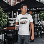 Man wearing a white t-shirt with a MGB car graphic and text, standing outdoors under a black umbrella.