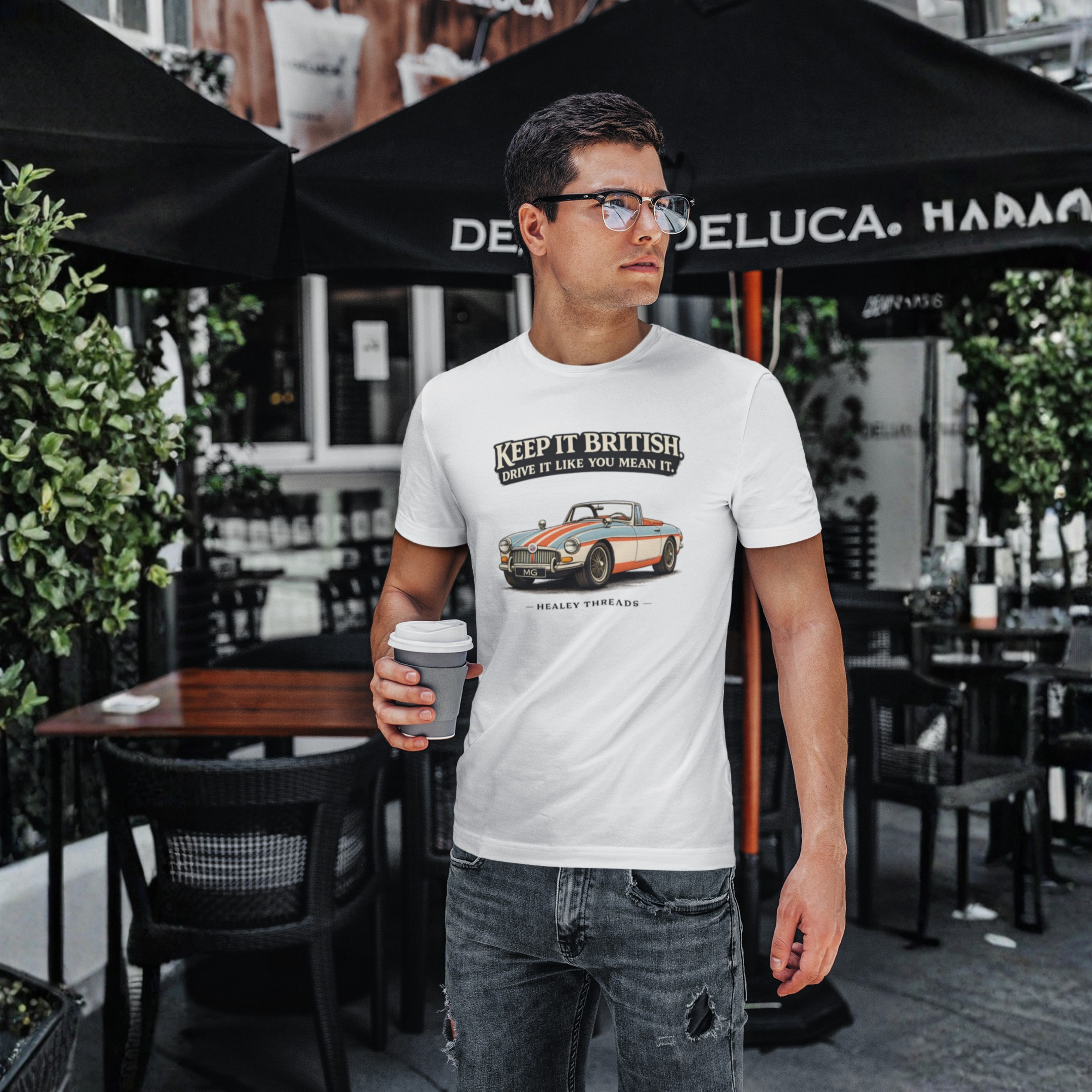 Man wearing a white t-shirt with a MGB car graphic and text, standing outdoors under a black umbrella.