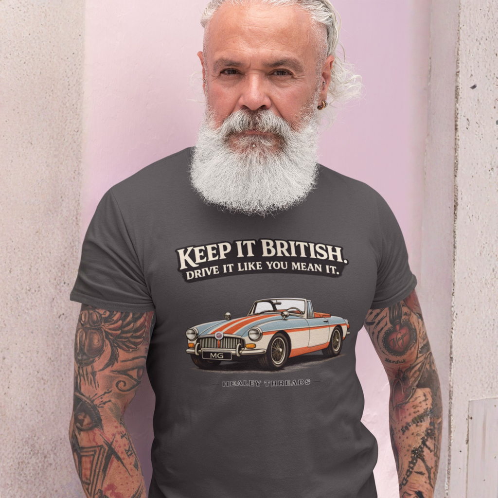 Man wearing a gray t-shirt with a MGB car graphic and text against a light pink wall.