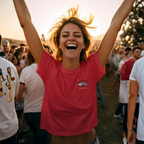 Woman in a red shirt with a Healey design on left chest with raised arms in a crowd at sunset