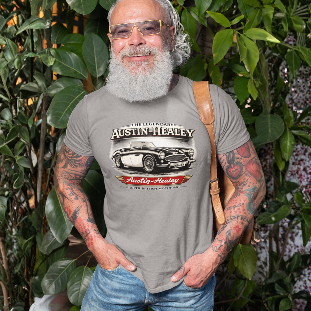 Man wearing a gray t-shirt with Austin-Healey logo, standing in front of green foliage.