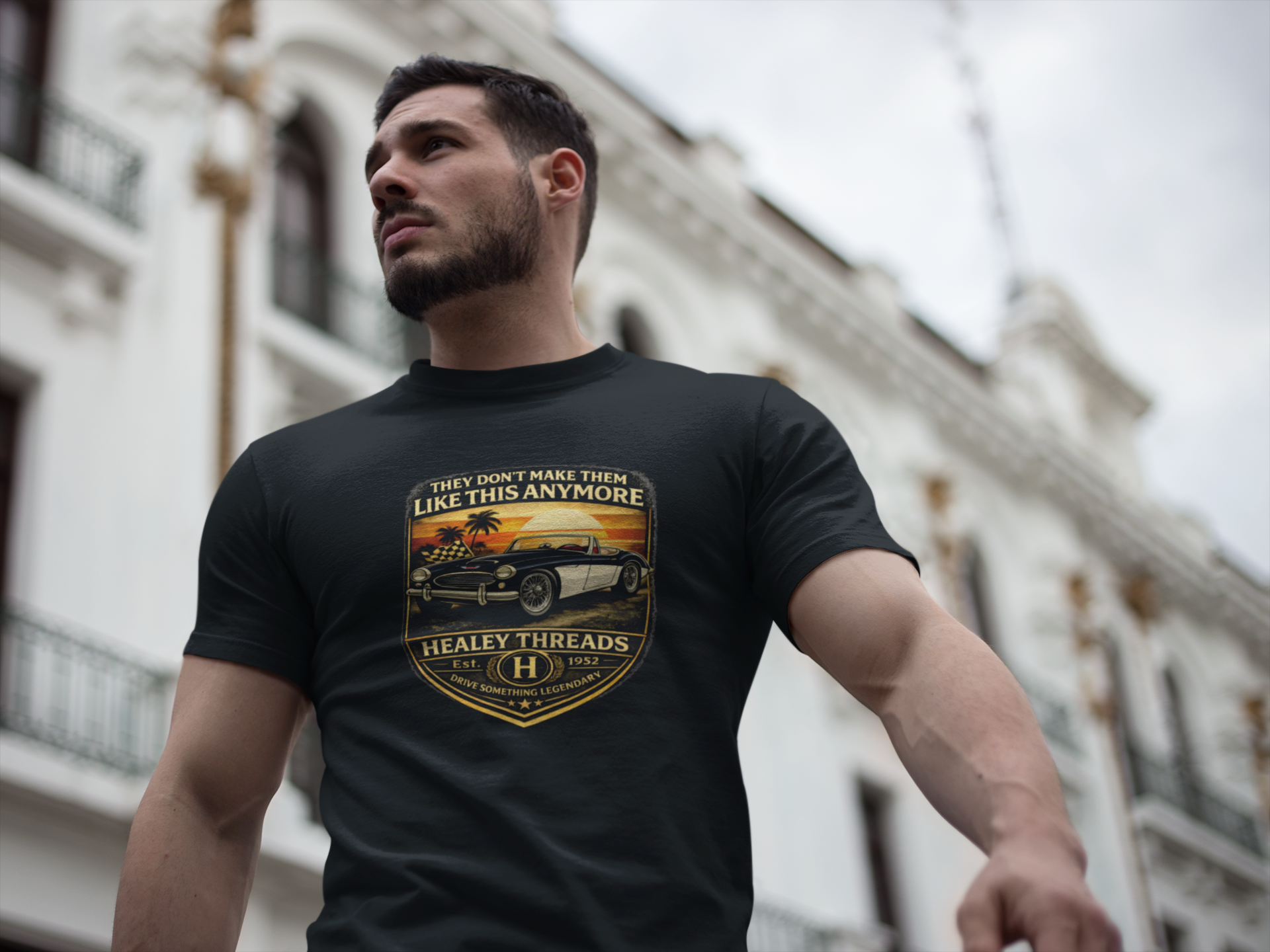 Man wearing a black t-shirt with a classic car design and text, standing in front of a building. 