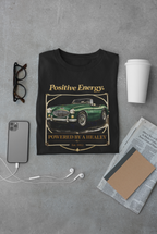Black t-shirt with vintage car graphic and 'Positive Energy' text on a gray surface with accessories.