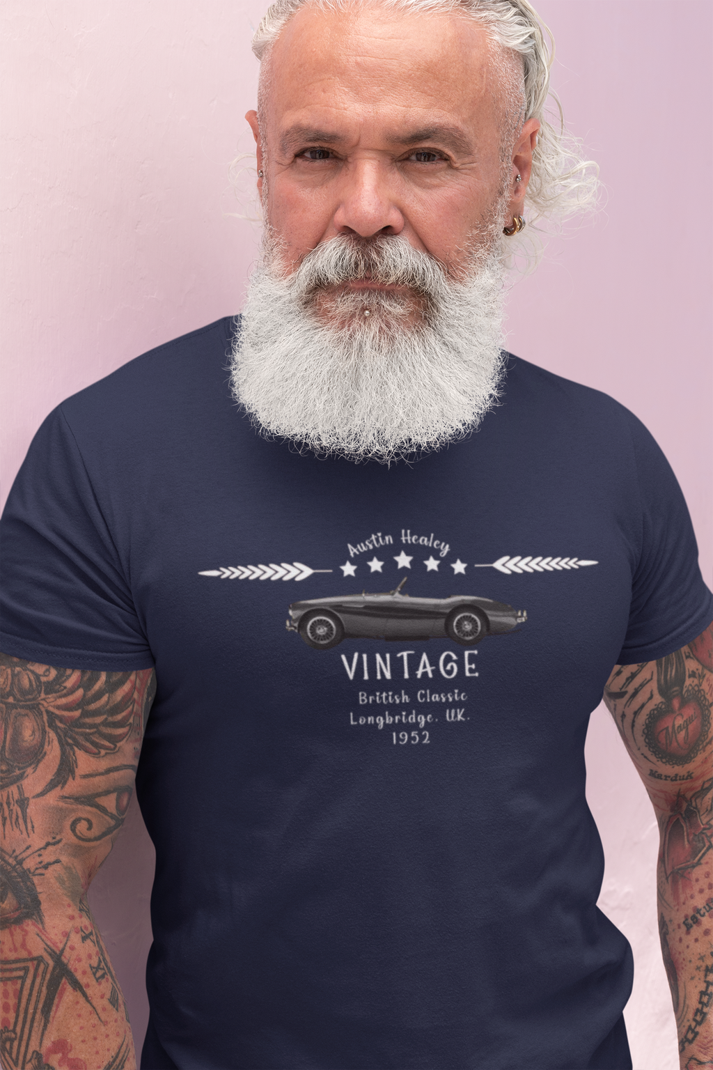 Man wearing a navy blue t-shirt with a vintage car design and text on a pink background