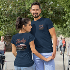 Man and woman wearing navy blue t-shirts with a vintage car design outdoors.
