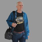 Man holding a black bag wearing a blue shirt and jeans on a gray background
