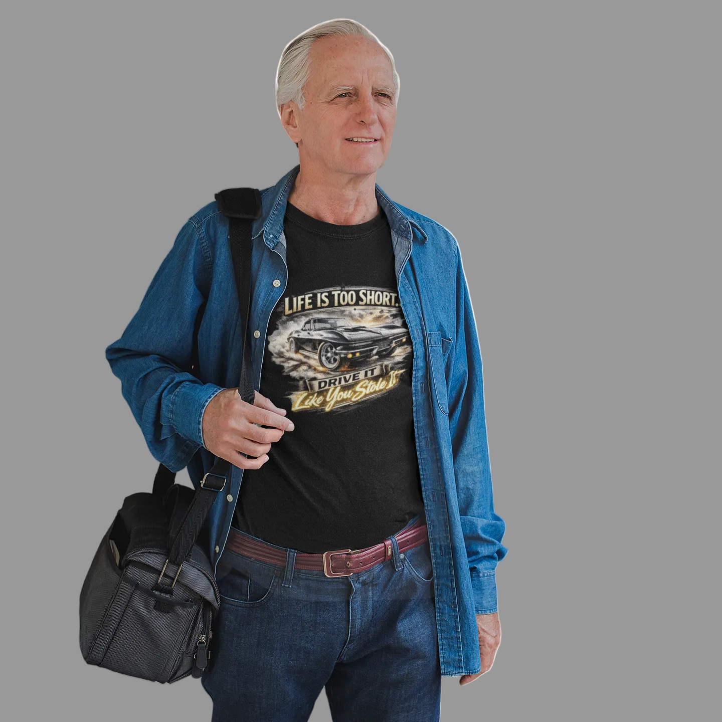 Man holding a black bag wearing a blue shirt and jeans on a gray background
