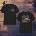 Front and back of a black t-shirt with Healey car design on a wooden surface with sunglasses and keys.