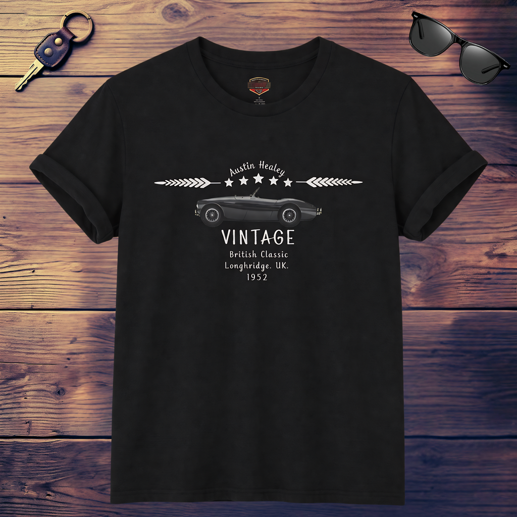 Black t-shirt with vintage Healey car design on a wooden surface with sunglasses and keychain.