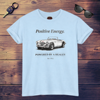 White t-shirt with a vintage car graphic and text on a wooden surface, accompanied by sunglasses and a key.